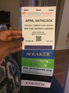 April's conference badge with ribbons for Speaker, Spectrum Scholar, pronouns she/her/hers, Wakanda Research Library Staff, and Council